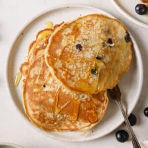 A plate of blueberry banana pancakes with a fork.