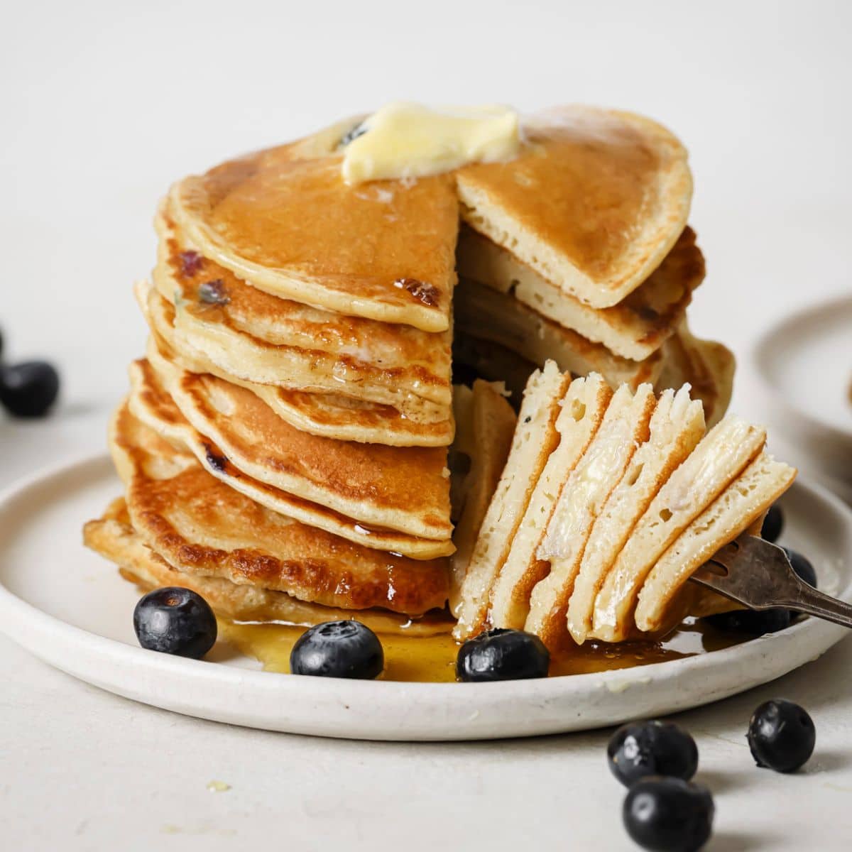 A forkful of blueberry banana pancakes served with butter, syrup and fresh blueberries.