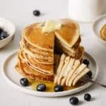 A forkful of blueberry banana pancakes served with butter, syrup and fresh blueberries.