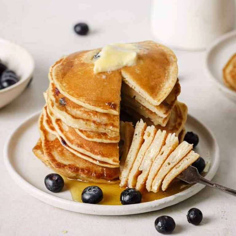 A forkful of blueberry banana pancakes served with butter, syrup and fresh blueberries.