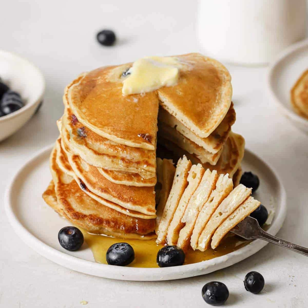 A forkful of blueberry banana pancakes served with butter, syrup and fresh blueberries.