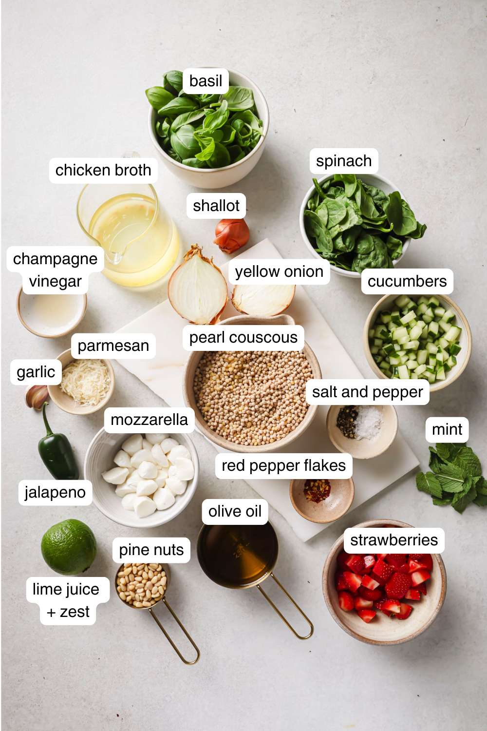Bowls of spinach, basil, couscous, strawberries, cucumbers, mozzarella near a lime, jalapeño and fresh mint.