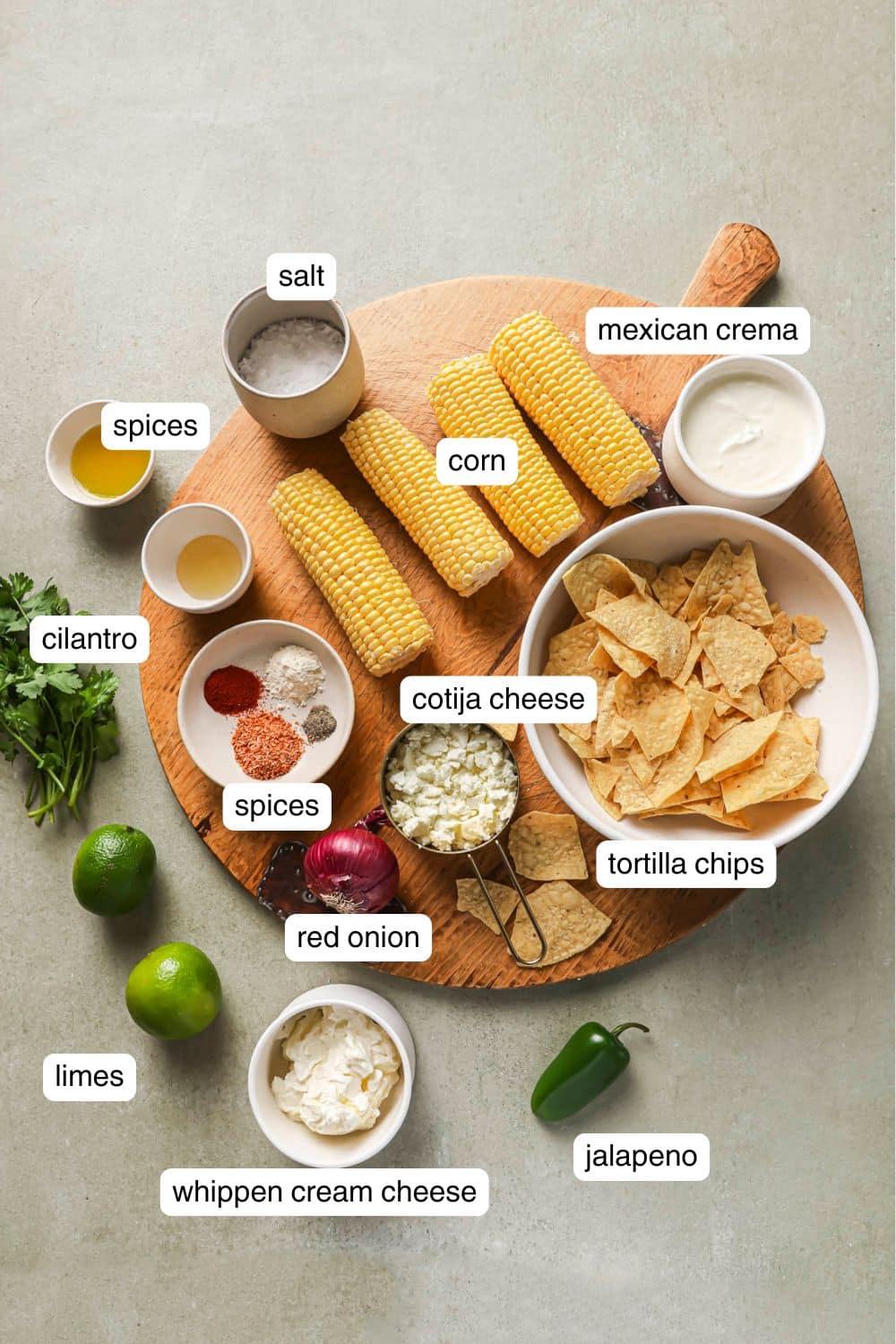 Ears of corn near bowls with spices, cheese, mayo and tortilla chips.
