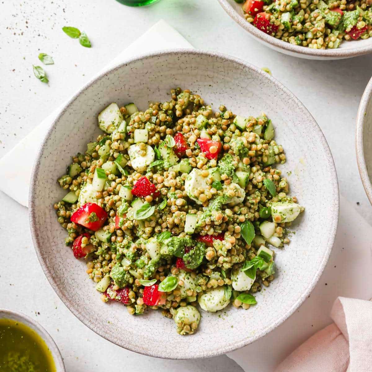 Israeli couscous salad topped with strawberries in a white bowl.