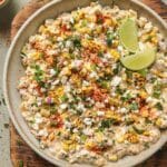 Mexican street corn dip in a bowl with two lime wedges.