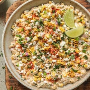 Mexican street corn dip in a bowl with two lime wedges.