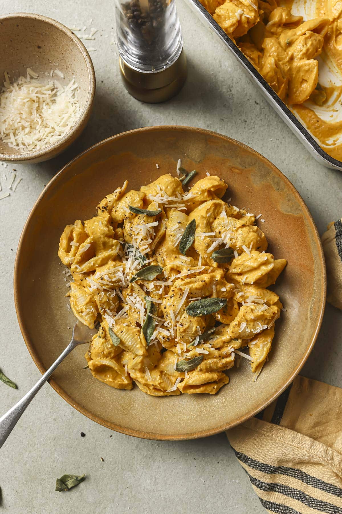 A bowl of baked feta pasta topped with parmesan cheese and fresh sage.