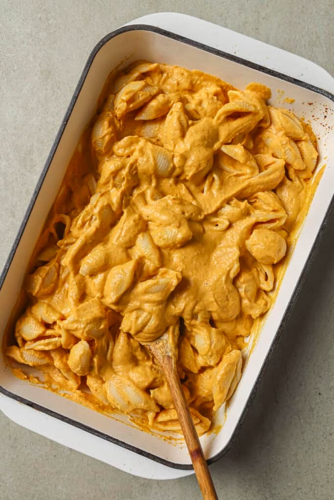 Mixing pasta with the sauce in a baking dish.