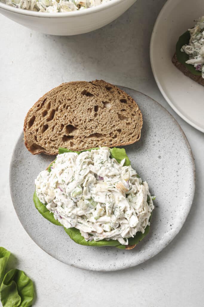 Adding lettuce and chicken salad to sliced bread on a plate.
