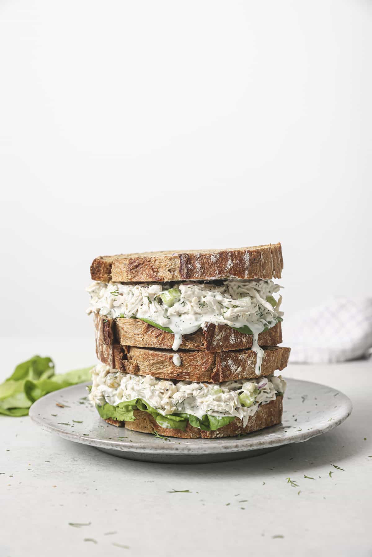 Two dill pickle chicken salad sandwiches stacked on a white plate.