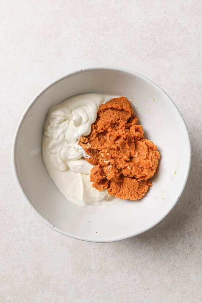 Pumpkin pie filling, whipped cream cheese and Cool Whip in a white bowl.
