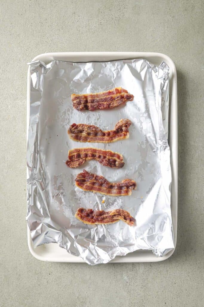 Slices of bacon on a foil lined baking sheet.