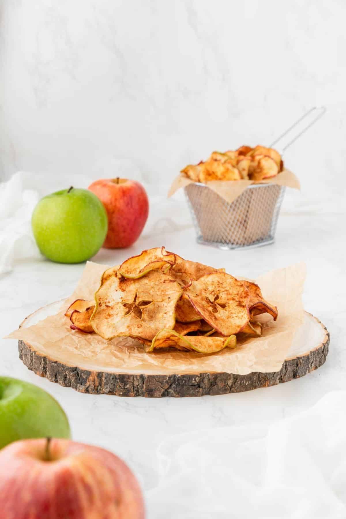 A wooden block with parchment paper and a pile of air fryer apple chips.