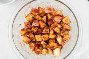 Coating apple chunks with spices in a glass bowl.