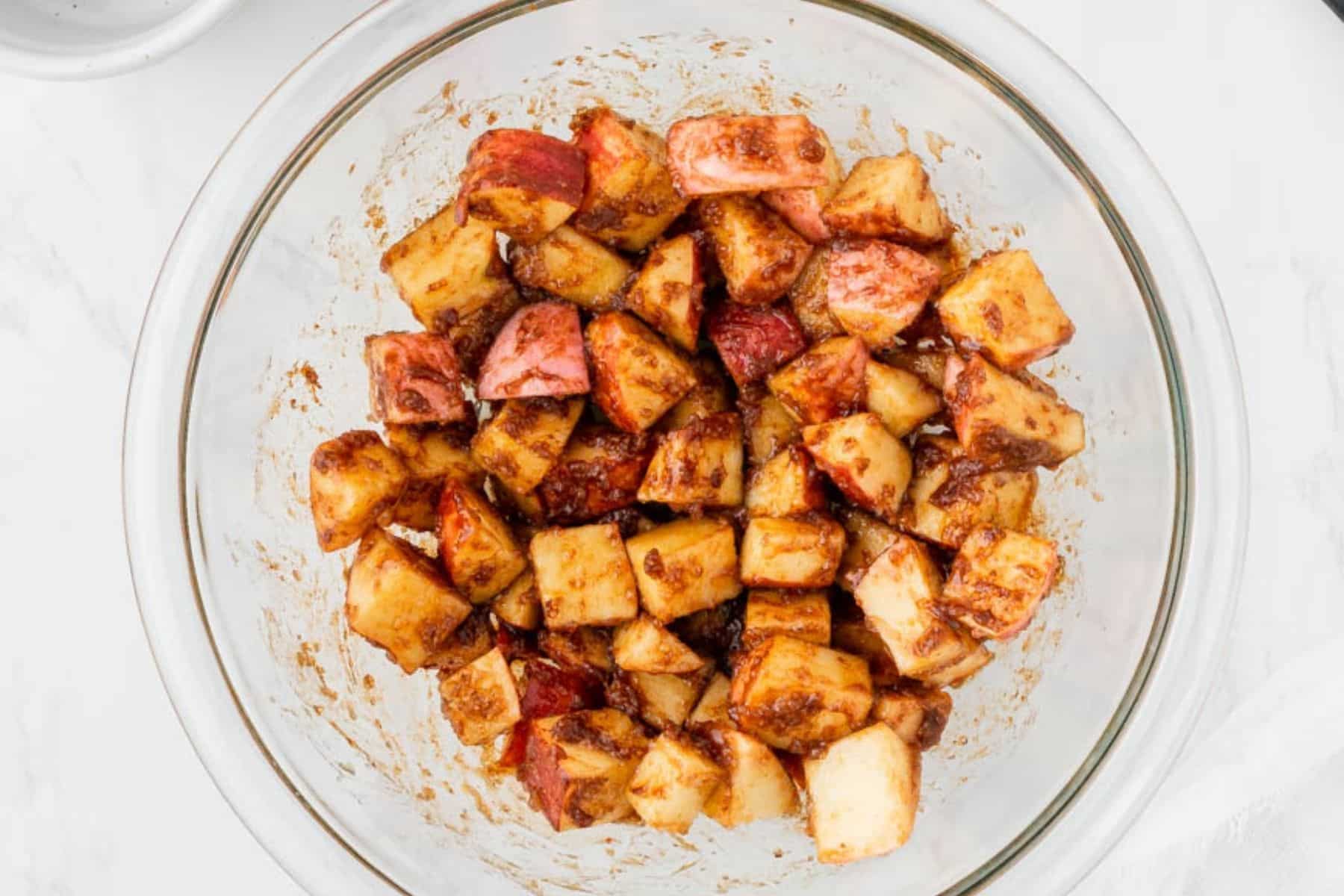 Coating apple chunks with spices in a glass bowl.