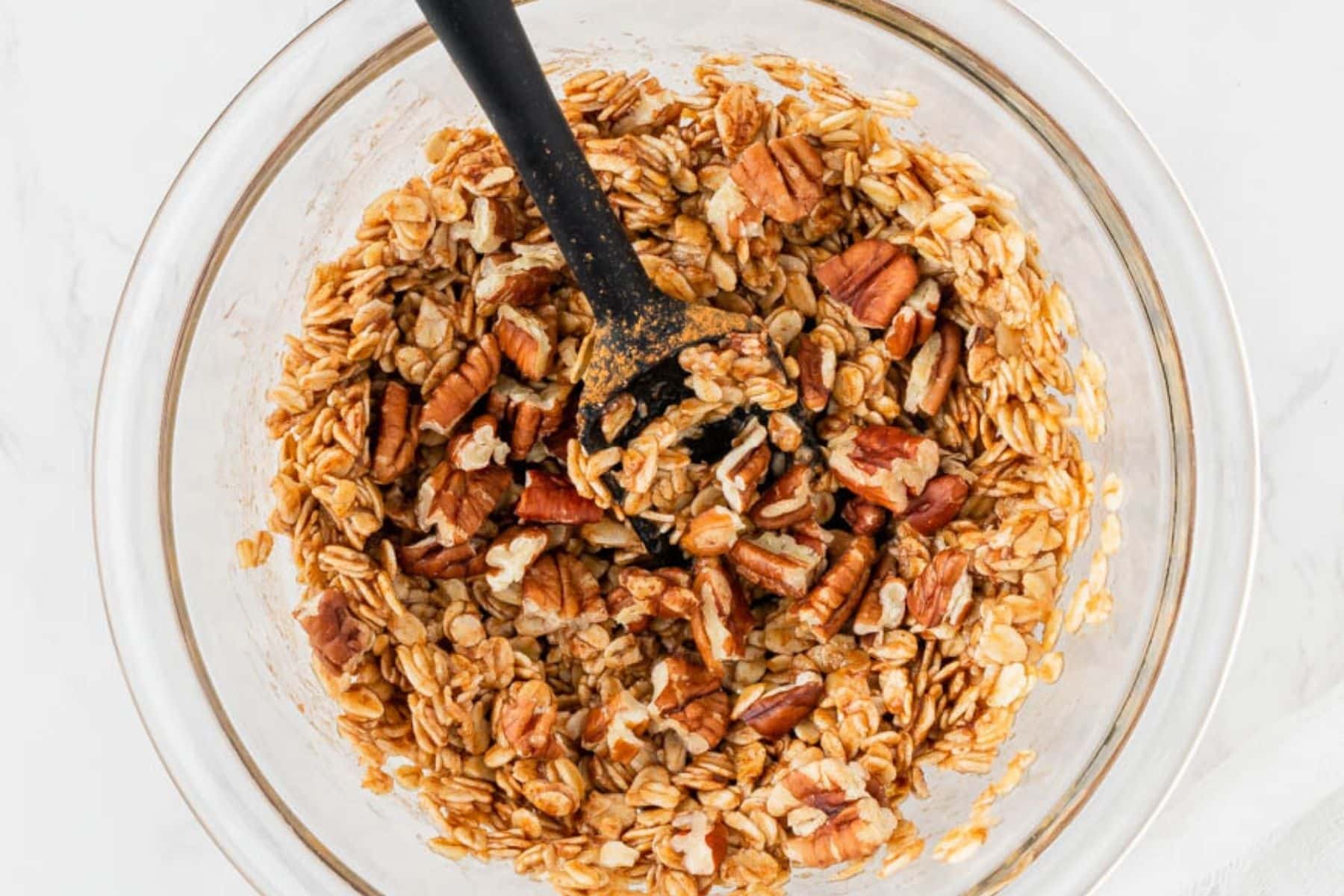 Mixing oats with pecans in a glass mixing bowl.