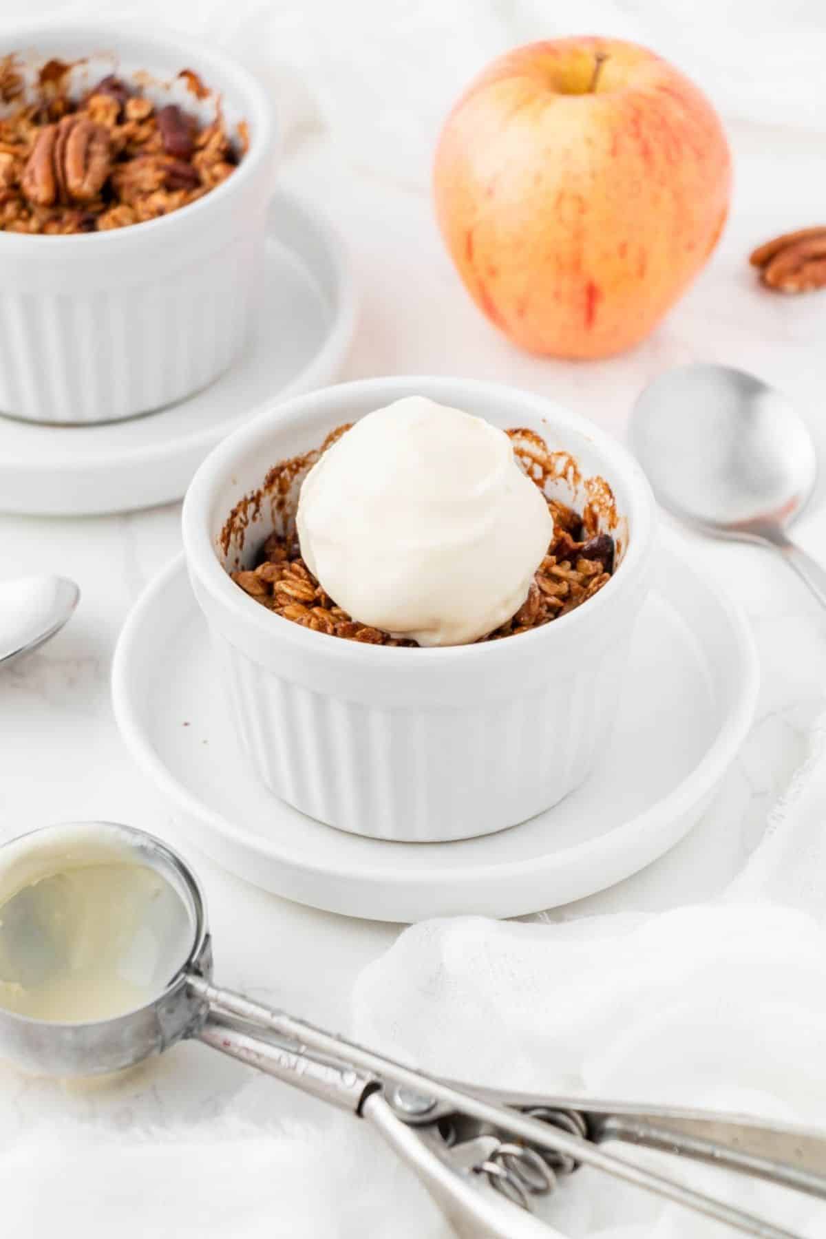 Air fryer apple crisp in ramekins with crunchy oat pecan topping and a scoop of vanilla ice cream.