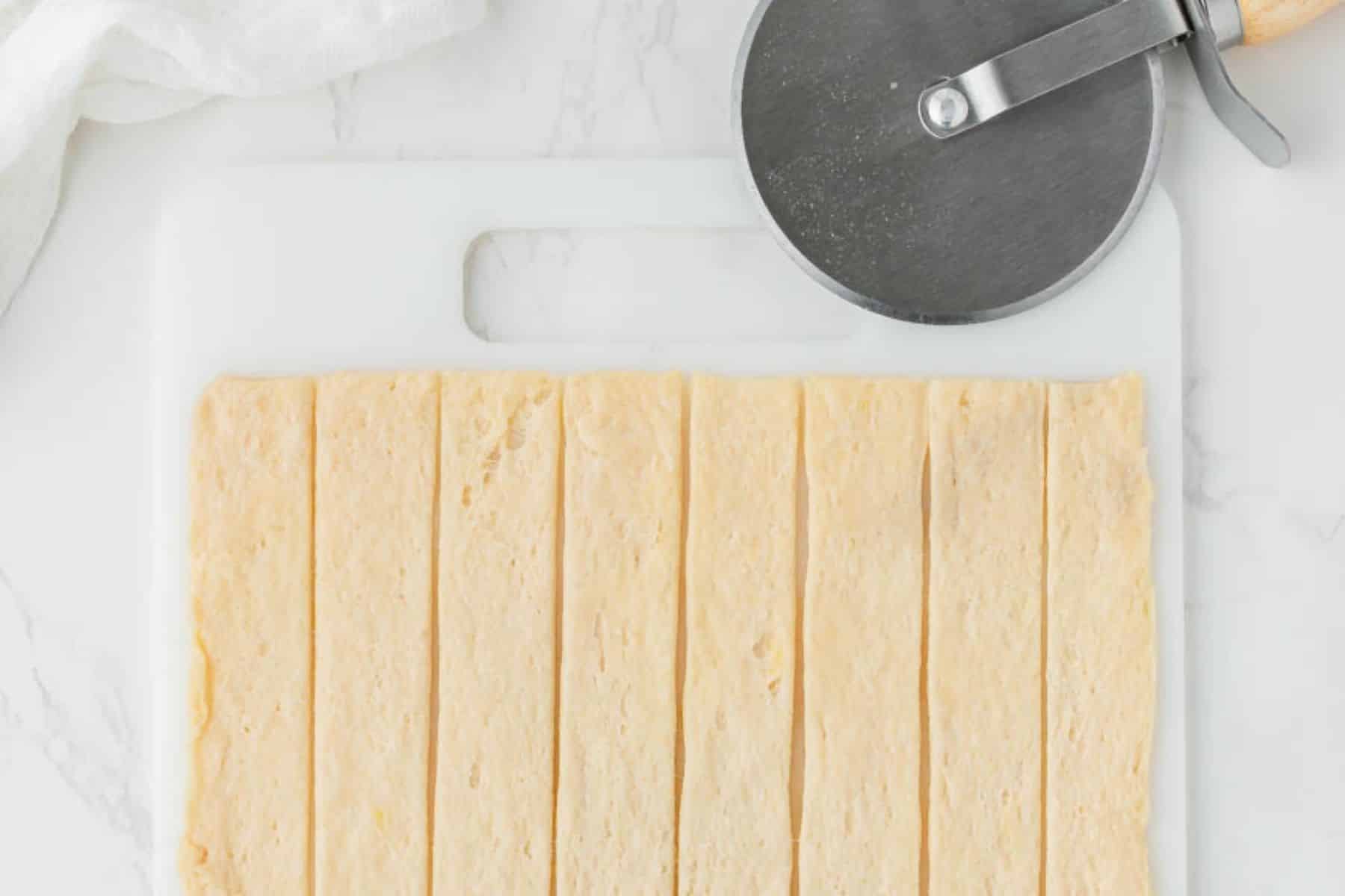 Cutting crescent roll dough into strips with a pizza cutter.