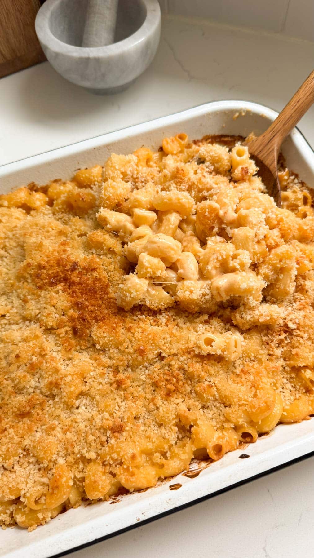 Buffalo mac and cheese in a white baking dish with a wooden serving spoon.