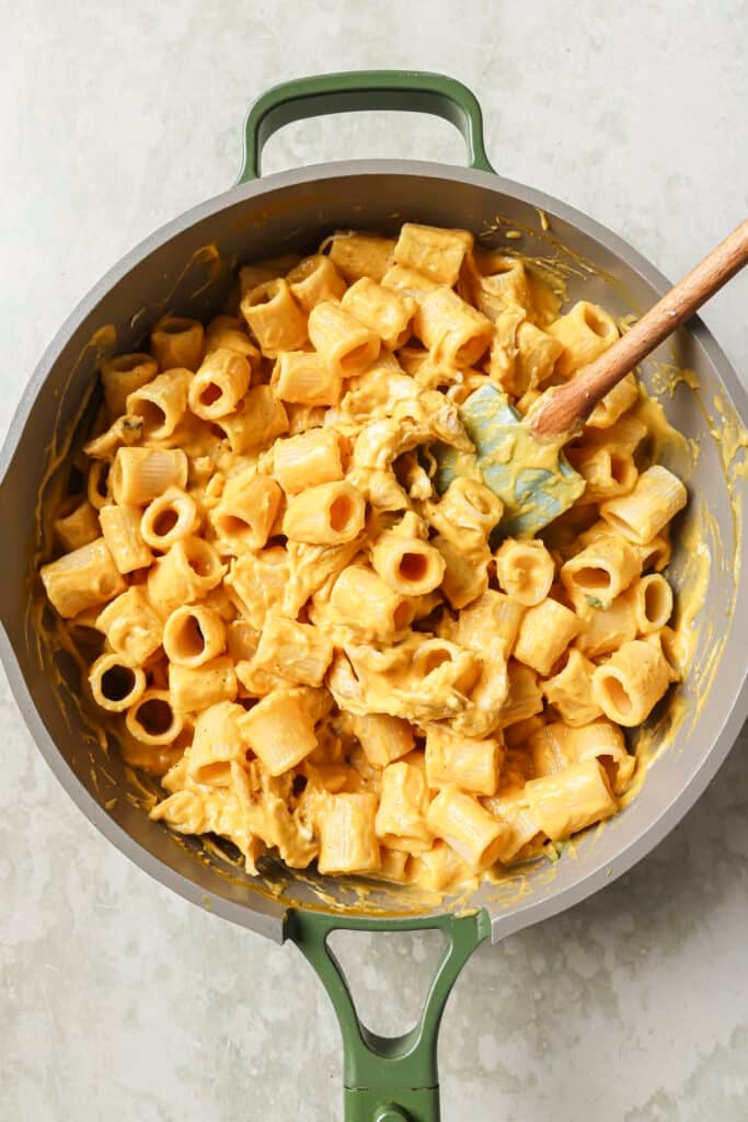 Stirring pasta with butternut squash sauce in a pan.