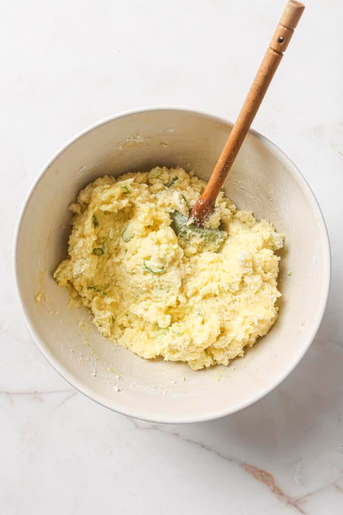 Stirring mashed potatoes with egg and flour in a white bowl.