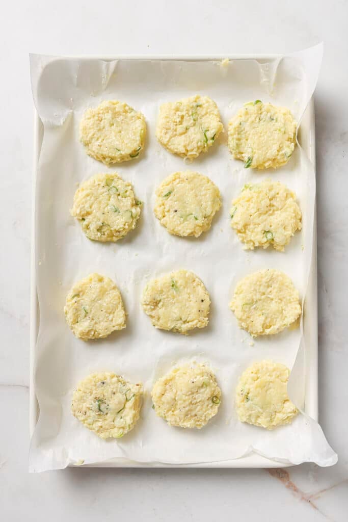 Mashed potato patties on a parchment lined baking sheet.