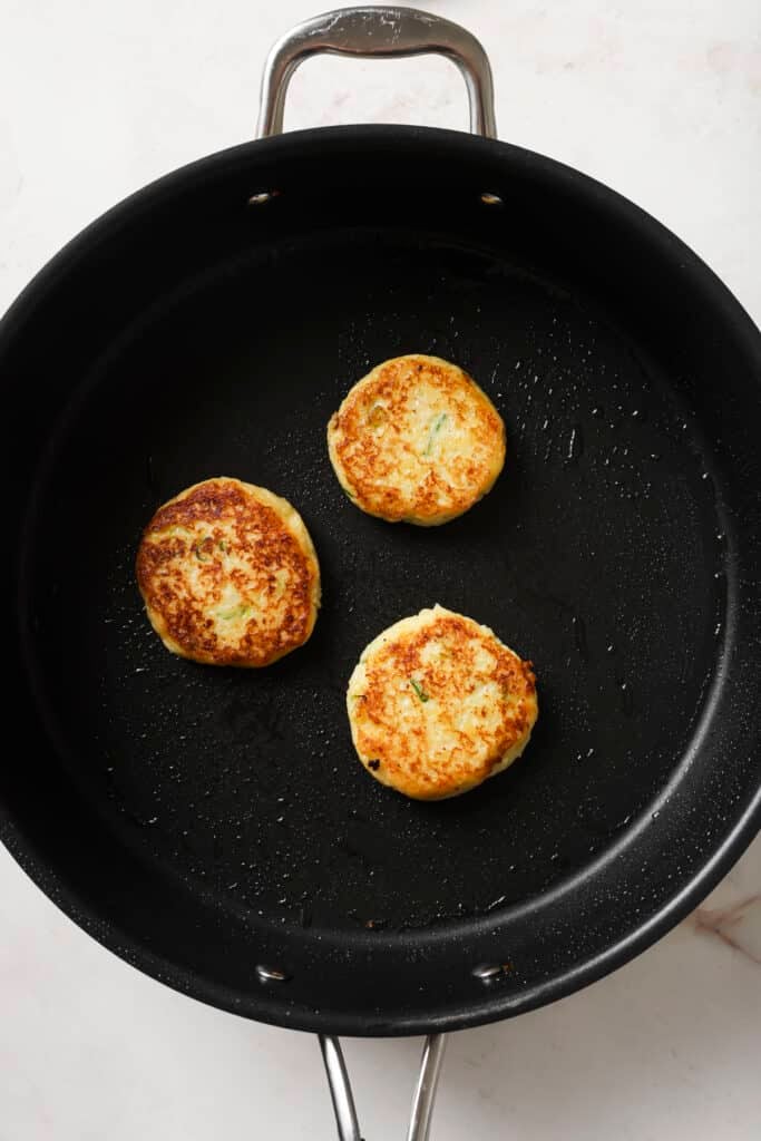 Searing potato cakes in a large skillet.
