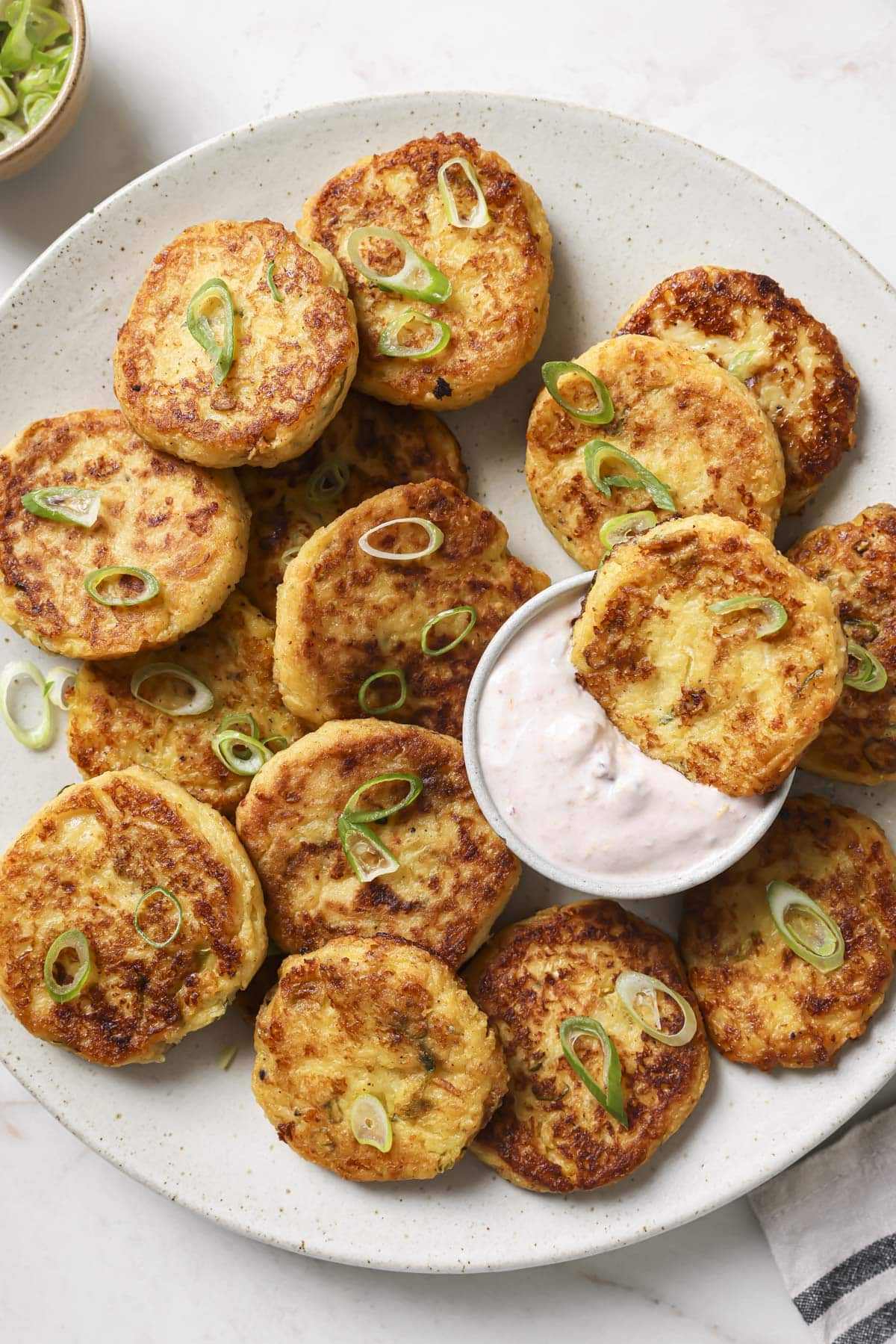 Loaded Mashed Potato Cakes on a plate with one dipped into a creamy cranberry sauce.