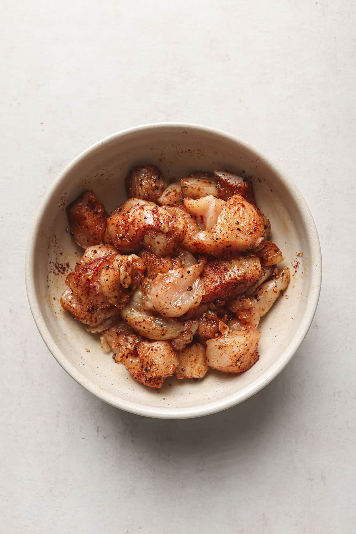 Pieces of chicken tossed with seasoning in a bowl.