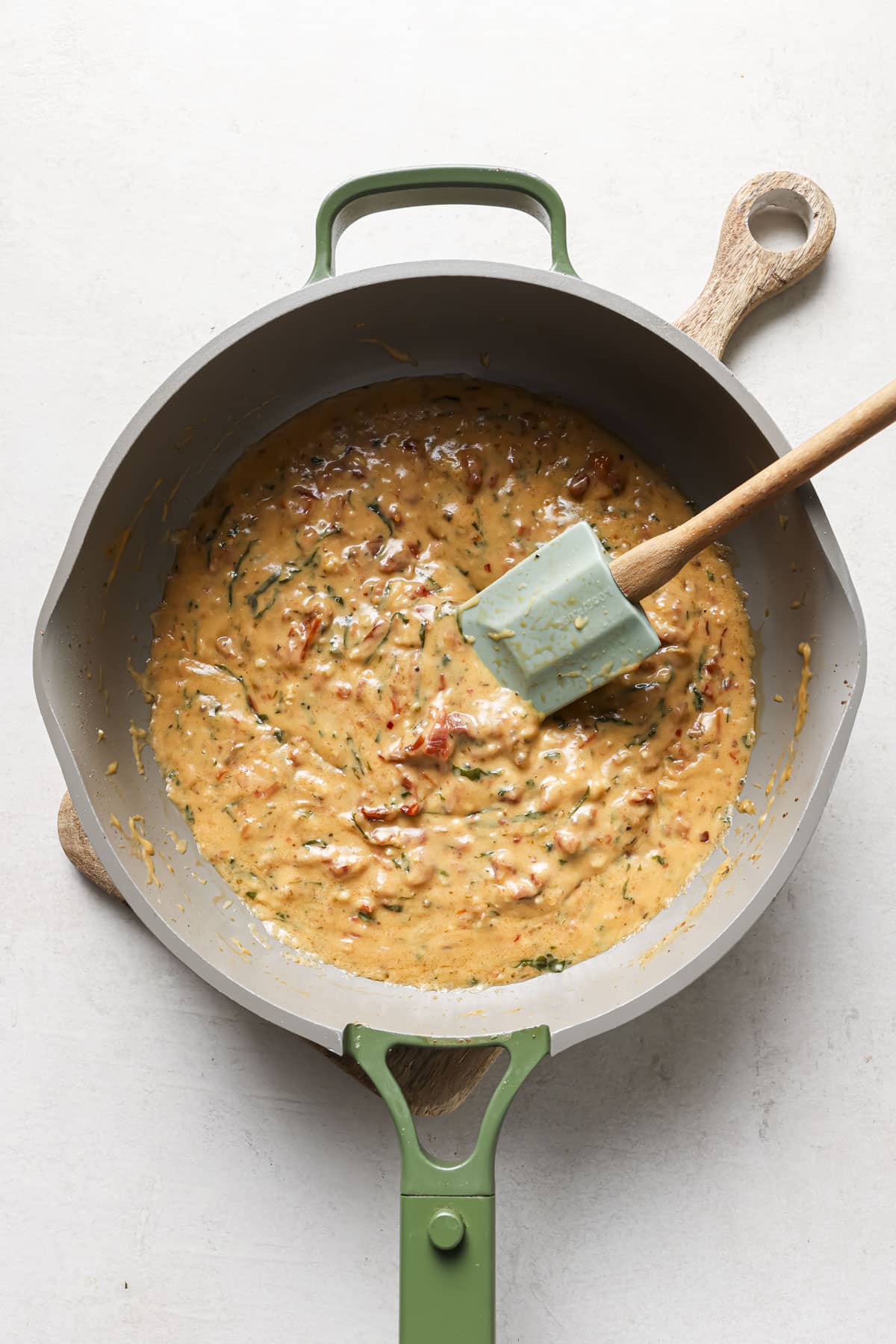 Stirring together a marry me chicken sauce in a large skillet.