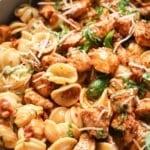 Close-up of pasta coated in creamy tomato basil sauce with chicken and fresh basil garnish.
