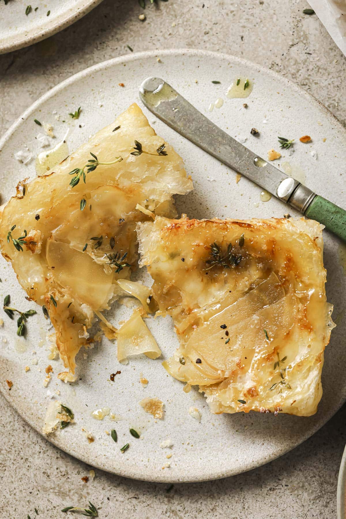 Puff pastry tart in half on a white plate with a knife.