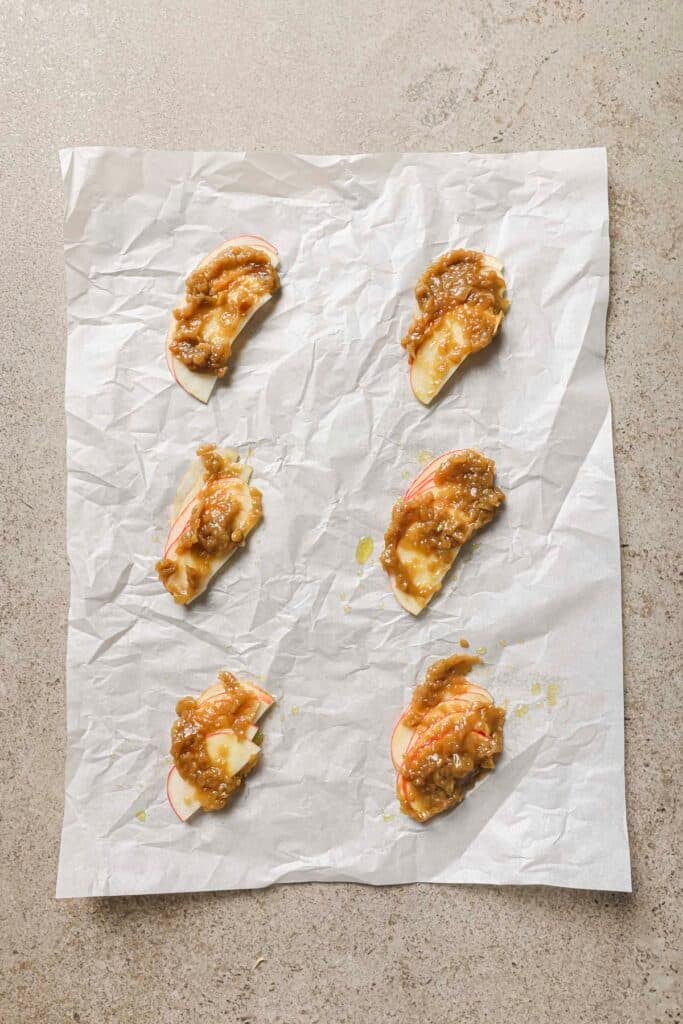 Thinly sliced apples with a topping of jam on parchment paper.