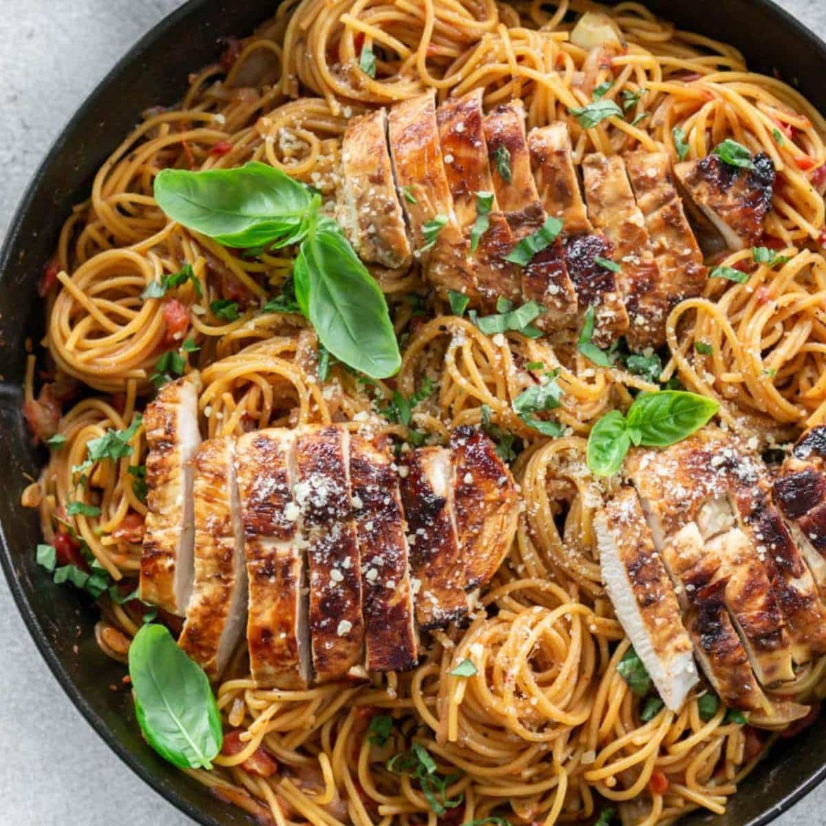 Sliced chicken over pasta in a skillet.