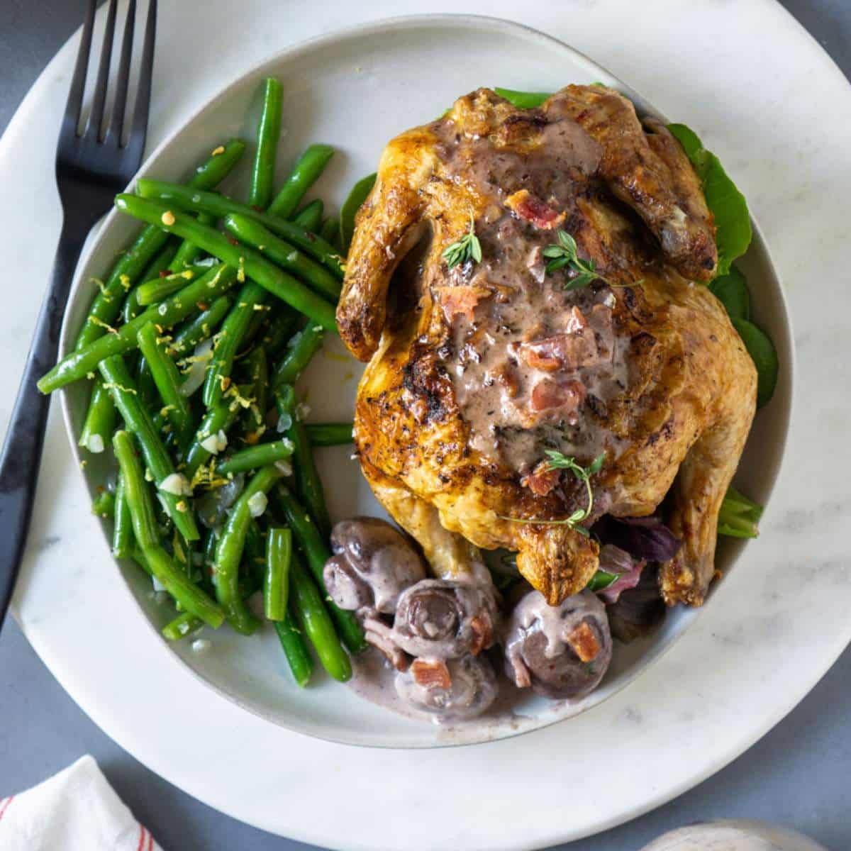 Green beans, a cornish hen, and mushroom gravy on a white plate with a black fork.