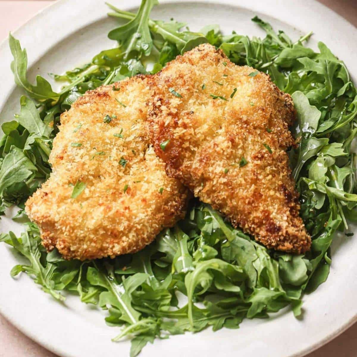 A plate of air fryer chicken cutlets served over greens.