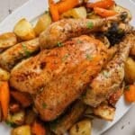 Slow roasted chicken on a platter with carrots and potatoes.
