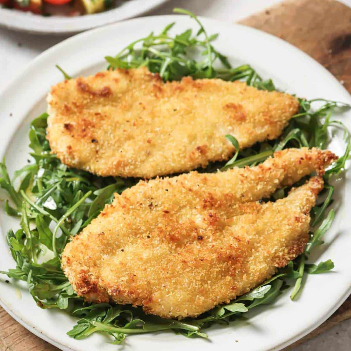 Chicken cutlets over arugula on a white plate.