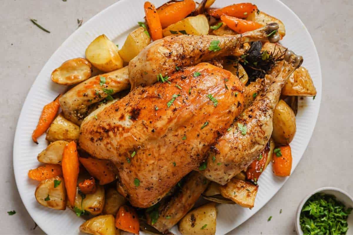Slow roasted chicken on a large white serving platter with carrots and potatoes.