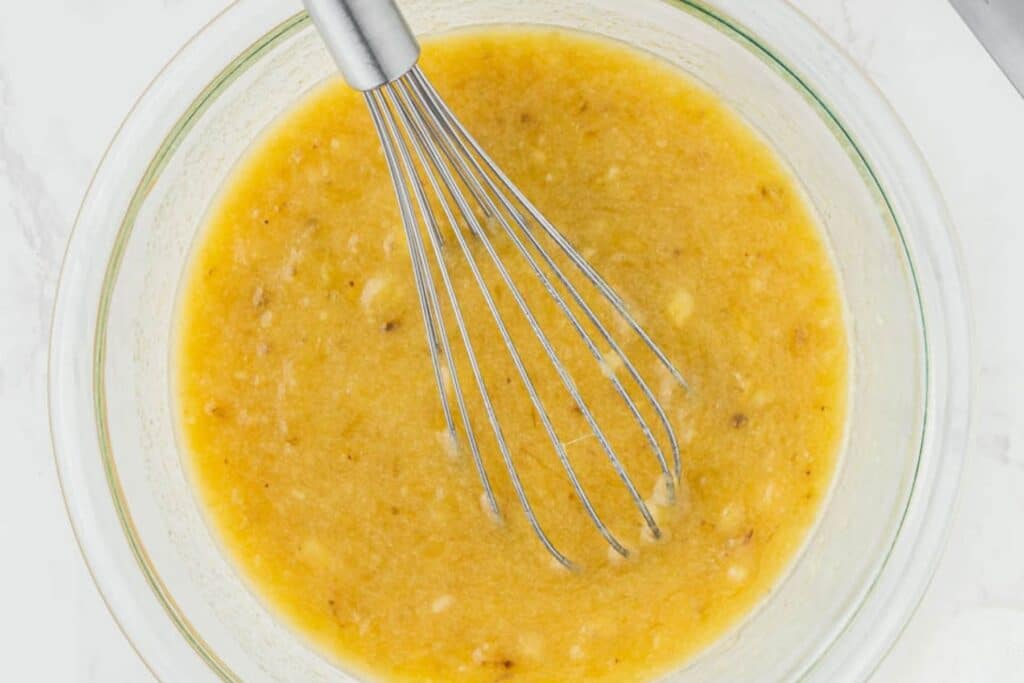 Mixing banana bread batter in a glass bowl.