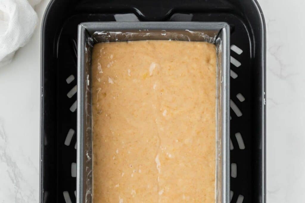 A baking pan with banana bread batter in the air fryer basket.