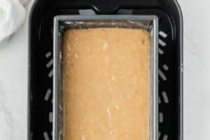 A baking pan with banana bread batter in the air fryer basket.