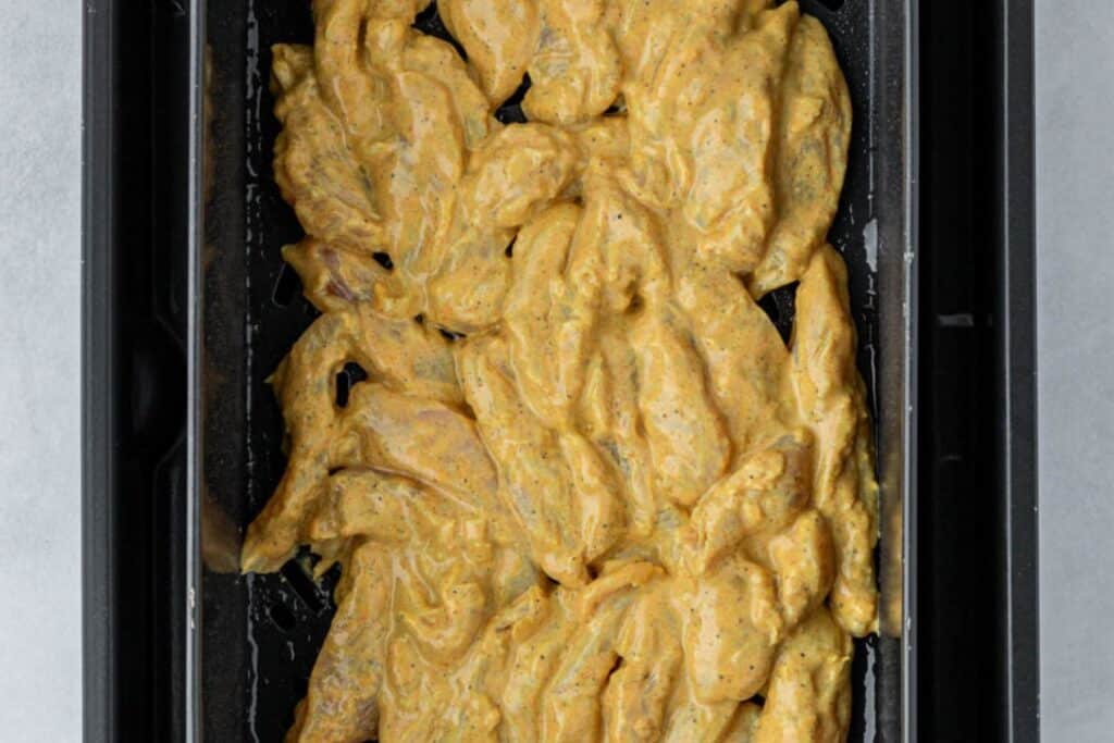 Marinated chicken in the air fryer basket.