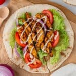 Top down view of a piece of pita bread with air fried chicken shawarma and fixins.