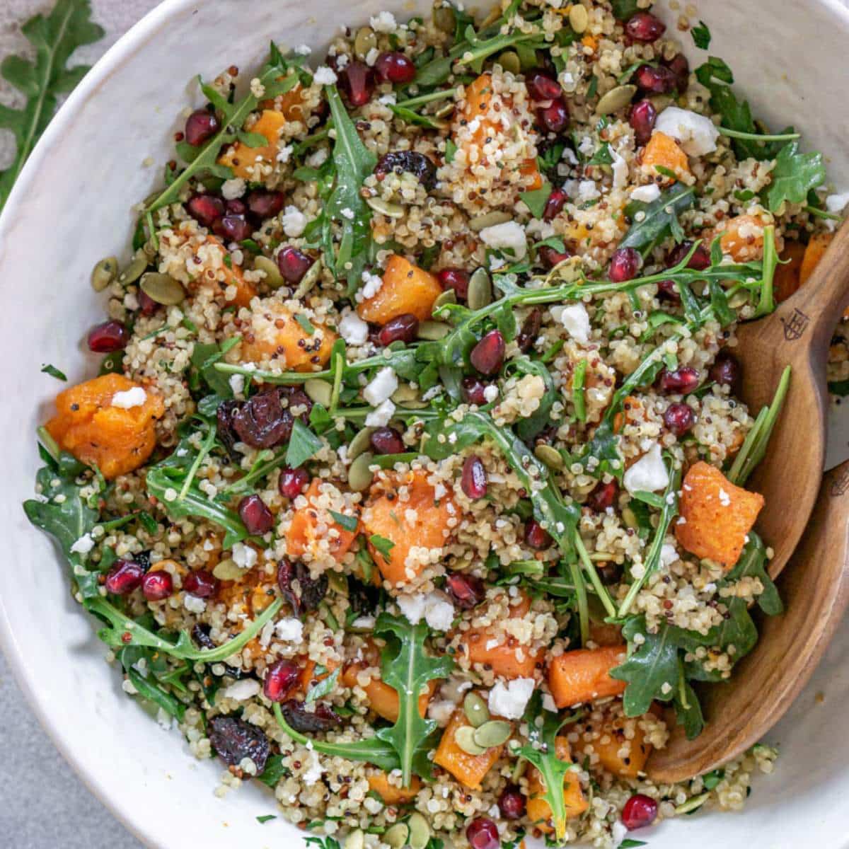 Cranberry quinoa salad in a bowl with wooden spoons.