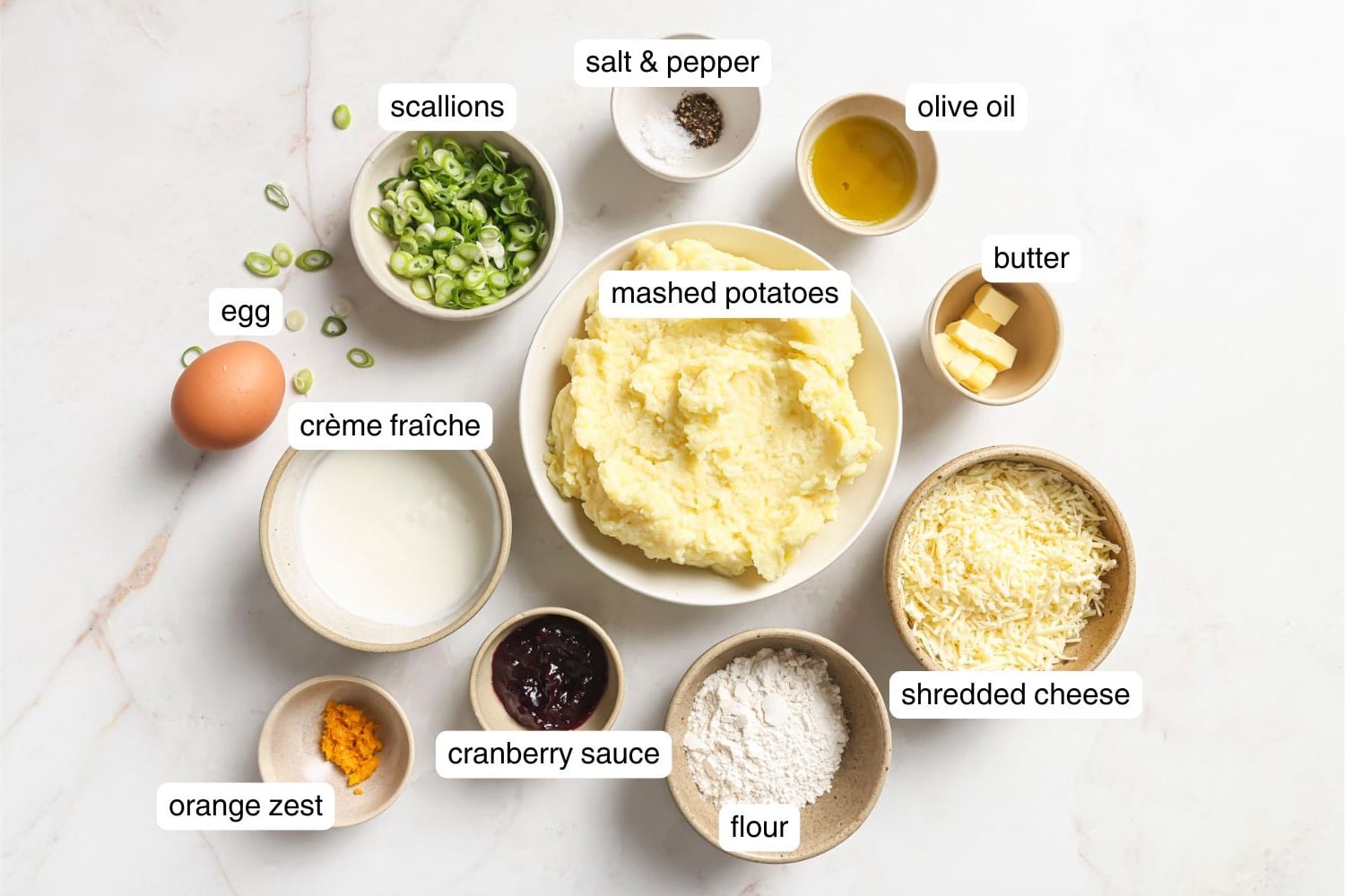 Small bowls with mashed potatoes, shredded cheese, flour, olive oil, cranberry sauce, and scallions.