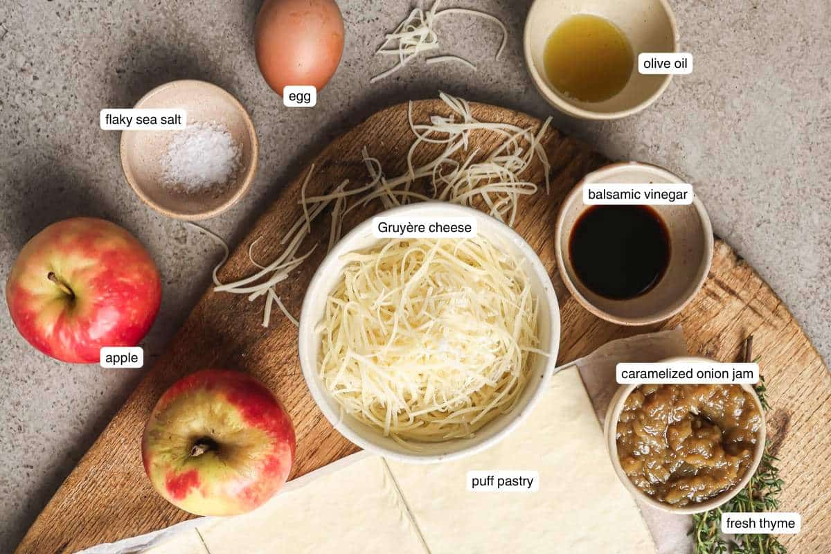 Apples and an egg near small bowls of grated cheese, sea salt, olive oil and onion jam.