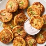 Loaded Mashed Potato Cakes on a plate with one dipped into a creamy cranberry sauce.