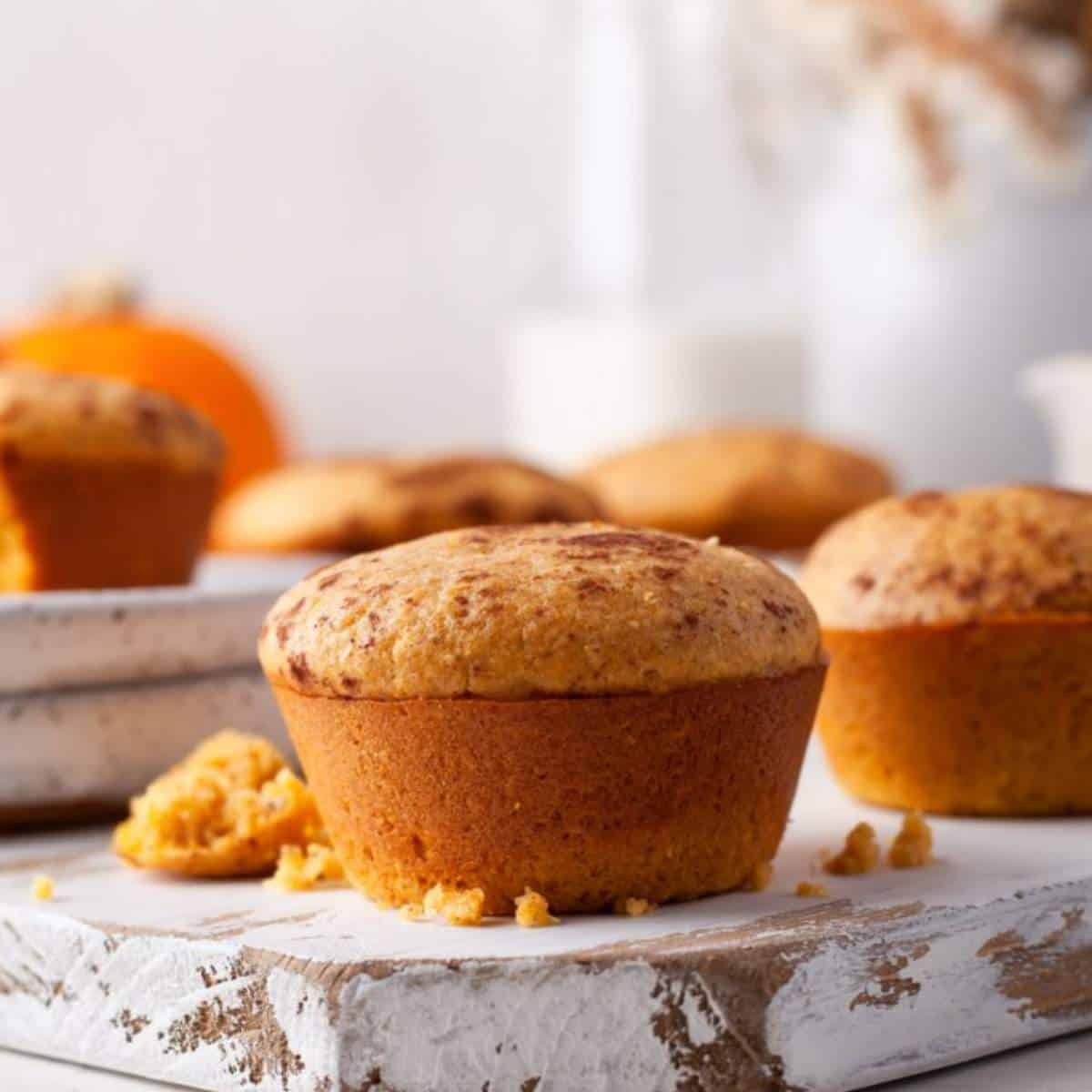 Pumpkin cornbread muffin on a wood board with milk behind.