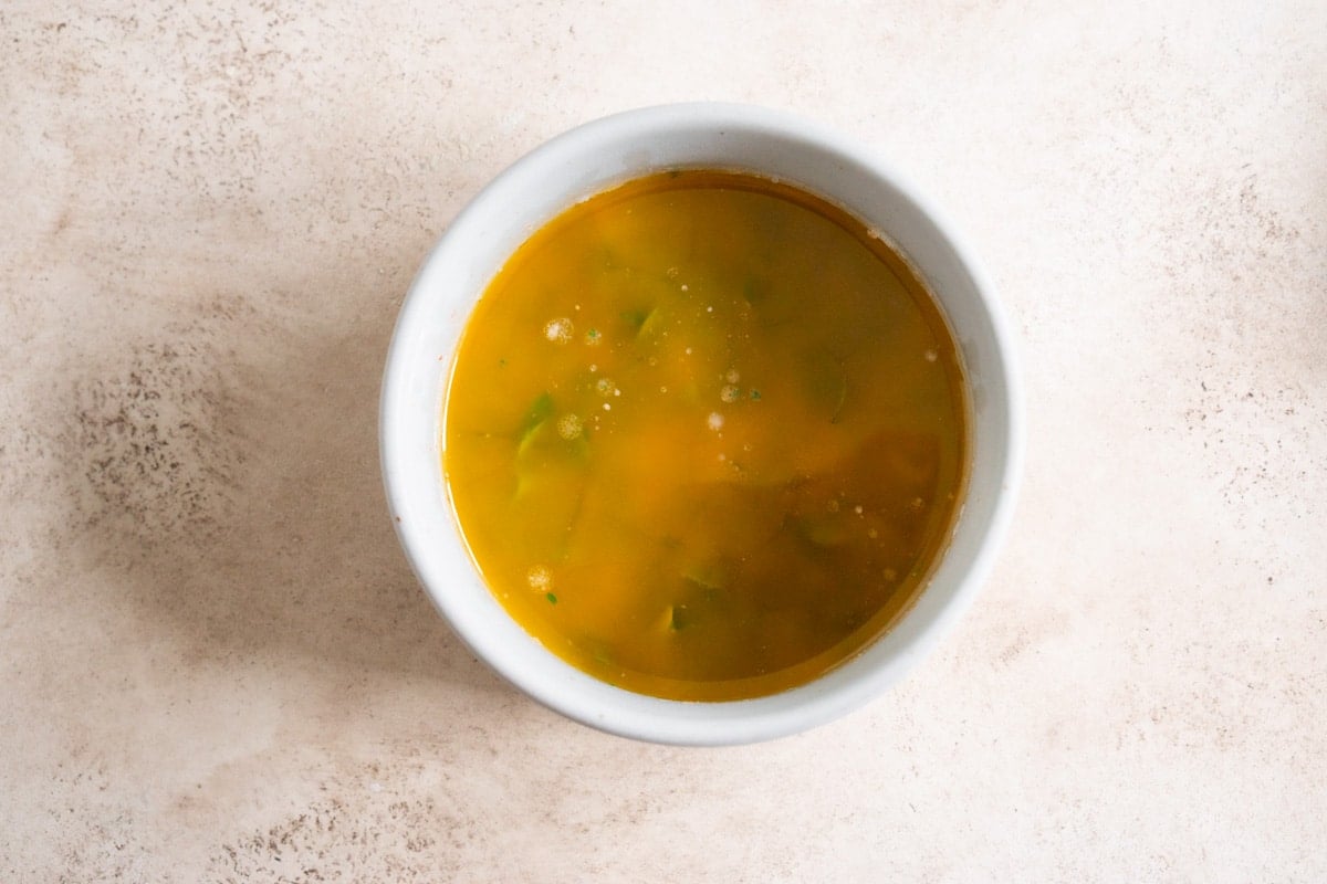 A mix of melted butter, garlic and lemon juice in a small white bowl.